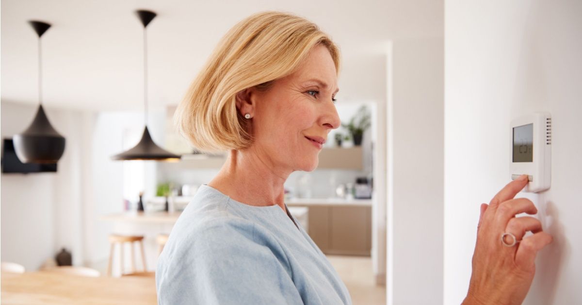 A woman easily adjusting her smart thermostat to control multi-zone underfloor heating from a wall-mounted unit
